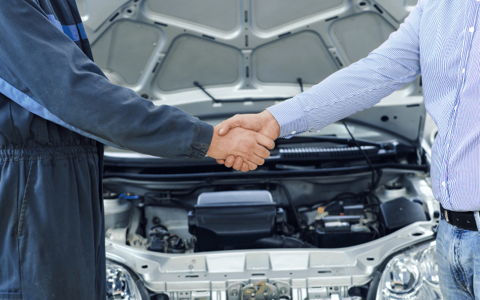 customer and technician shaking hands in front of a car with open bonnet